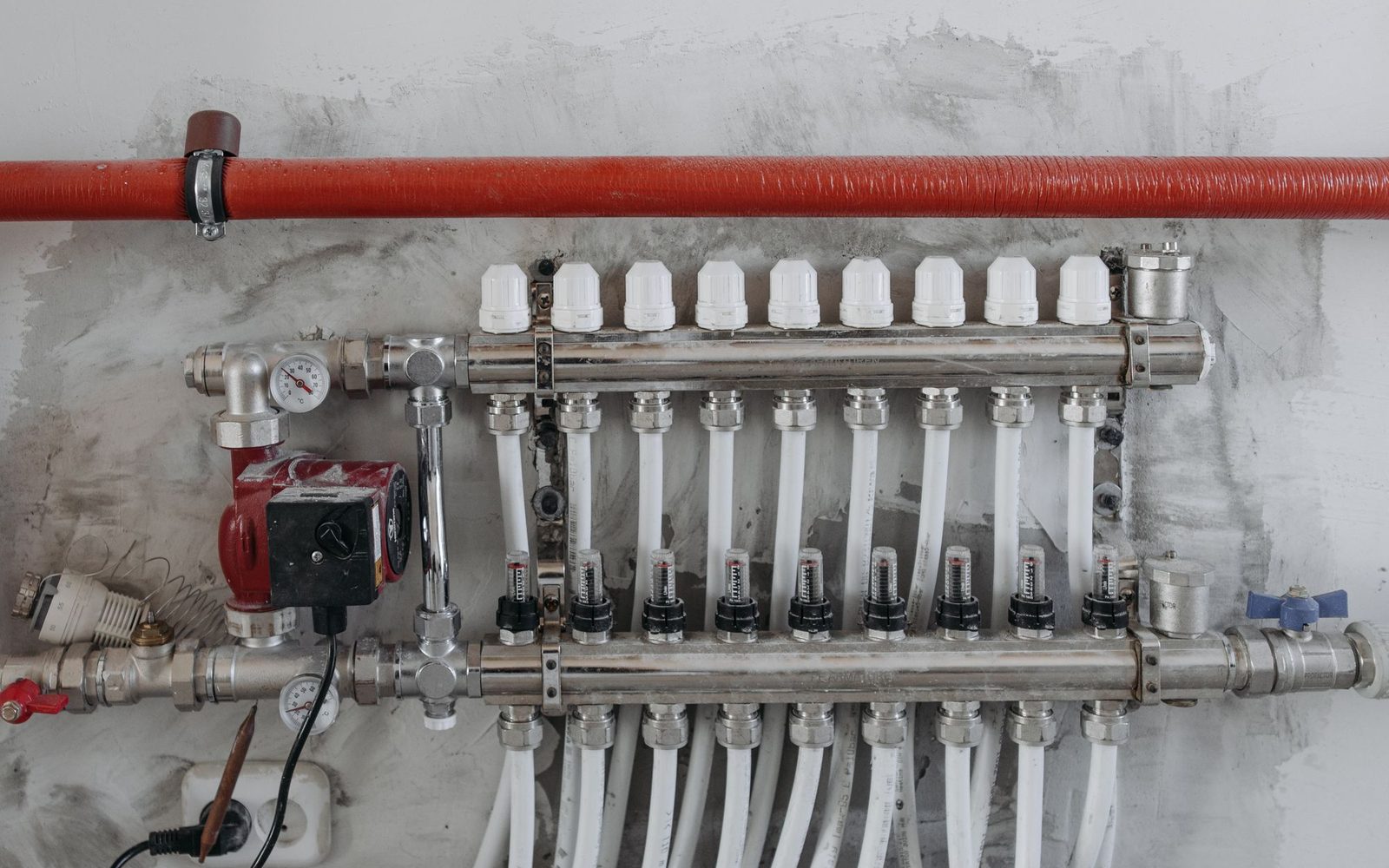Red circulating pump beside a stainless manifold and white supply tubes.