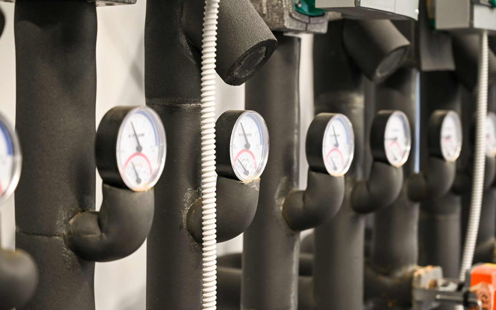 Pressure gauges on insulated pipes in a mechanical room.